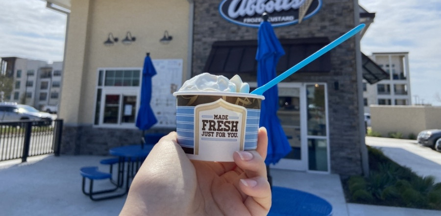 Hand holding up cup of frozen custard with spoon in it in front of the new Abbott's Frozen Custard location in Kyle