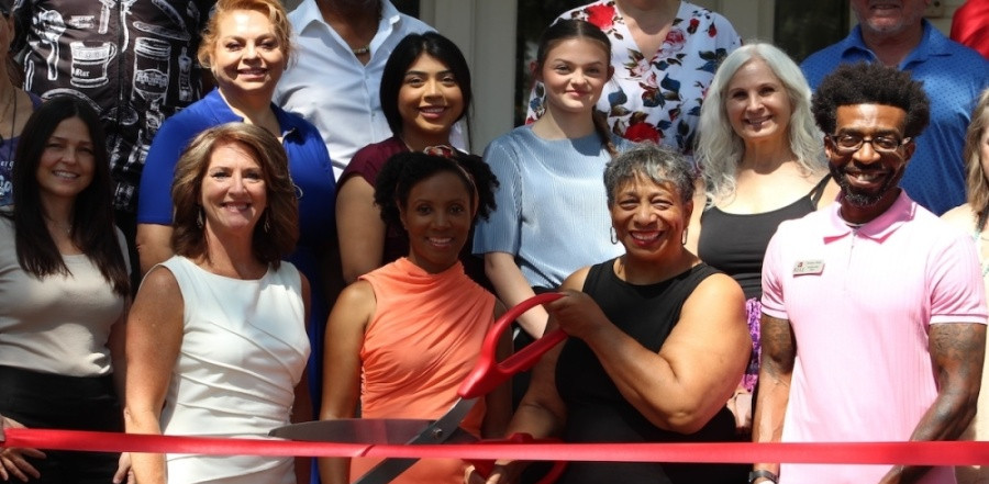 Crowd of people posing with large scissors cutting ribbon