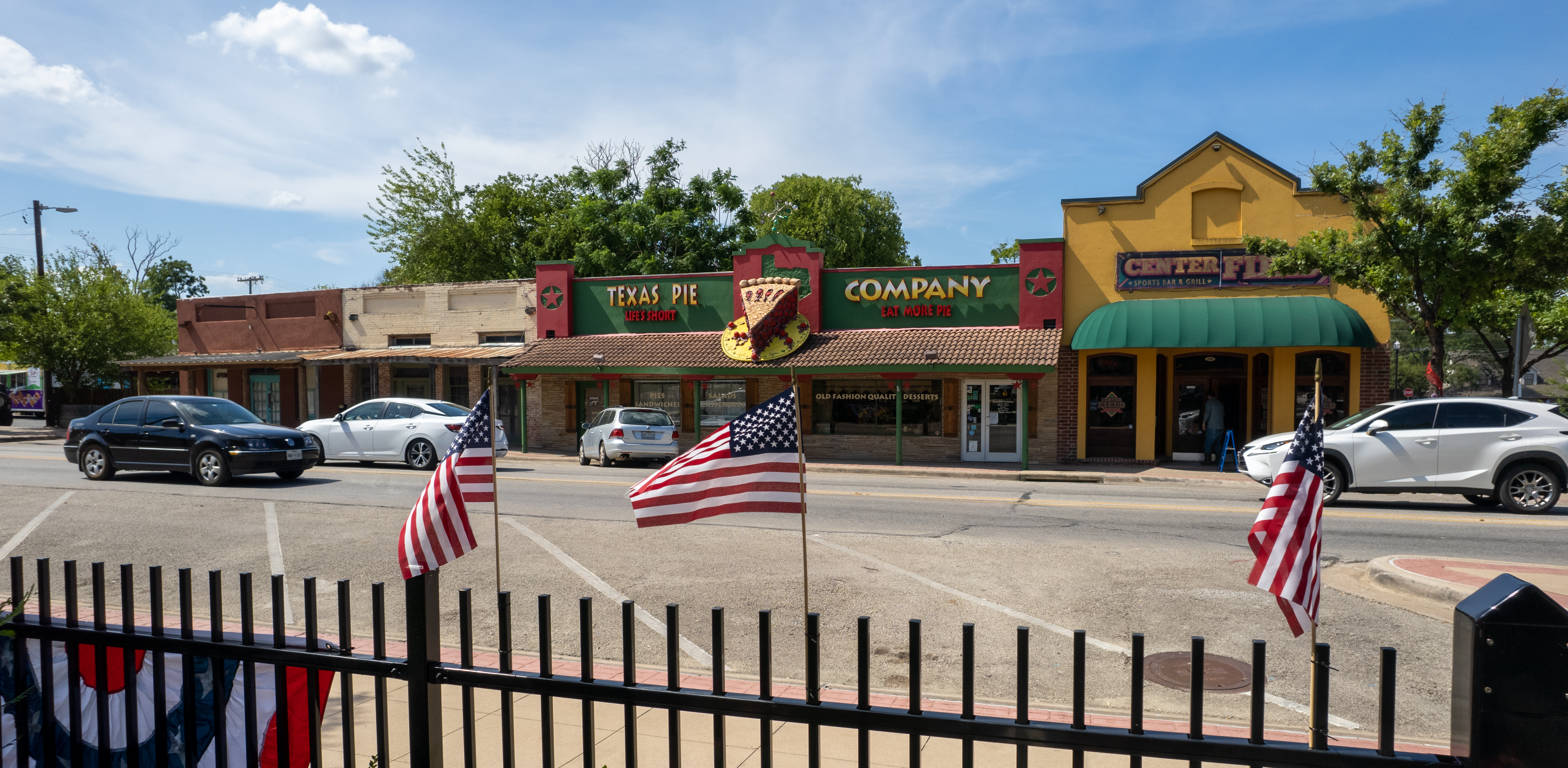 Row of Kyle downtown businesses with park fence in foreground.