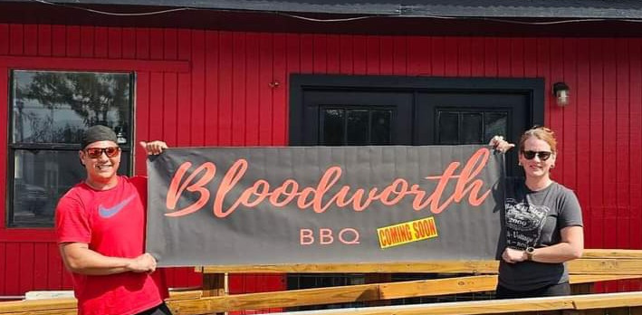 Thomas and Laticha Bloodworth holding up Bloodworth BBQ Coming Soon sign outside Bloodworth BBQ in downtown Kyle.