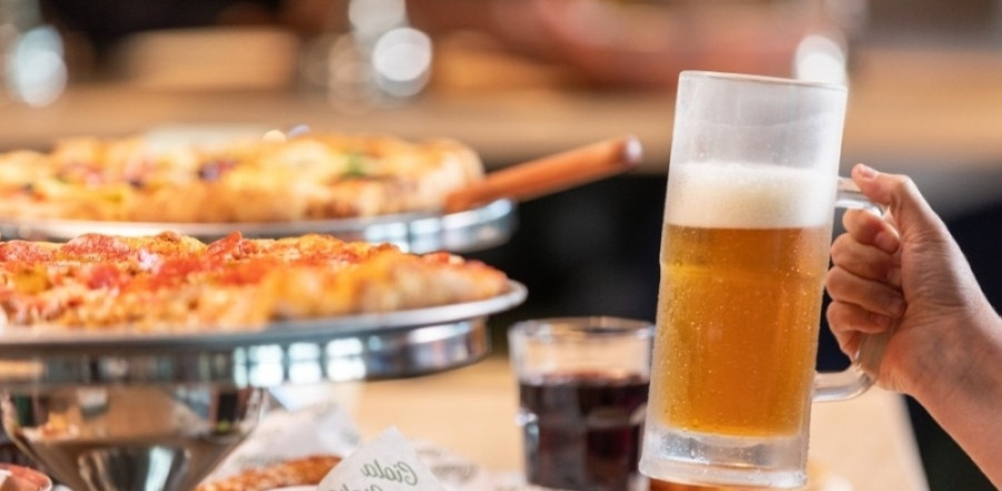 hand holding beer mug with table with pizza and salad on it in the background.